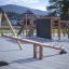Gungbräda Seesaw Nature på lekplats med klättervägg och rutschbanor i bakgrunden.