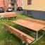Bänkbord dubbel i trä utomhus, placerade i en trädgård framför ett flerbostadshus.