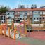 Epsilon lekplats med trästrukturer framför skolbyggnad.