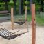 Double Hammock på sandig lekplats med trästolpar i bakgrund.