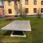 Fristående betongbordtennisbord på gräsmatta framför byggnad.
