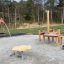 Lekplatsutrustning Daisy i sandlåda, med klätterstruktur och gunga i bakgrunden.
