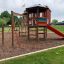 Klätterställning för barn med röd rutschkana och klättervägg i en park.