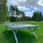 Bordtennisbord Outdoor i stål, placerat på gräsmatta i park.
