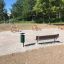 Bänk (HPL) i en parkmiljö med träd och utomhusanordningar.