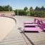 Tre solstolar Lounge Solstol i rosa vid en träpromenad nära en sandstrand.