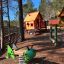 Rött lekstuga Skojiga Huset på en lekplats omgiven av träd.